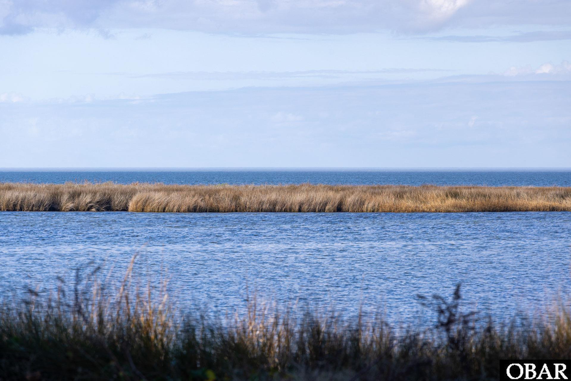 Waterfront lot with marsh grass separating a calm inlet from the open ocean.