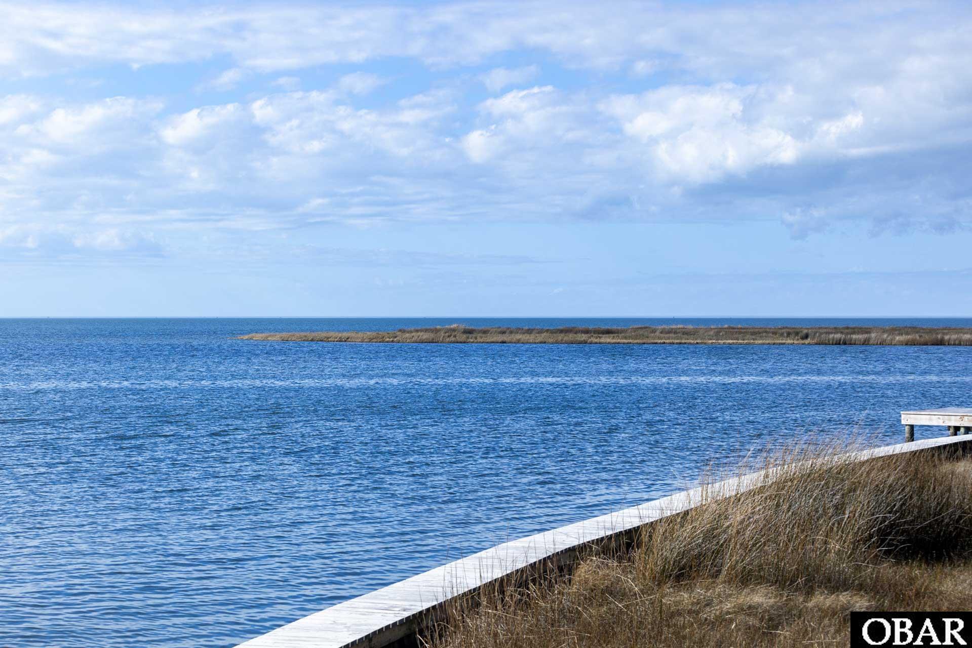 Waterfront lot with a wooden boardwalk, tall grasses, and a marshy island across the water.