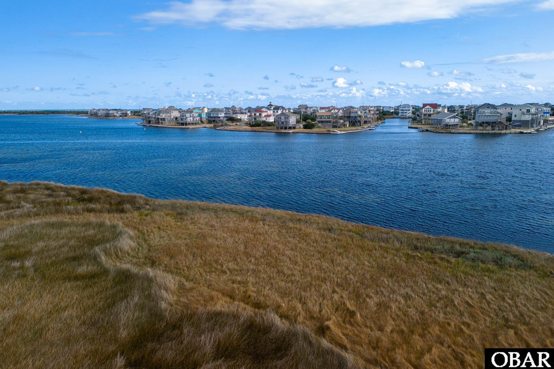 Aerial view of a grassy waterfront lot across from a coastal neighborhood.
