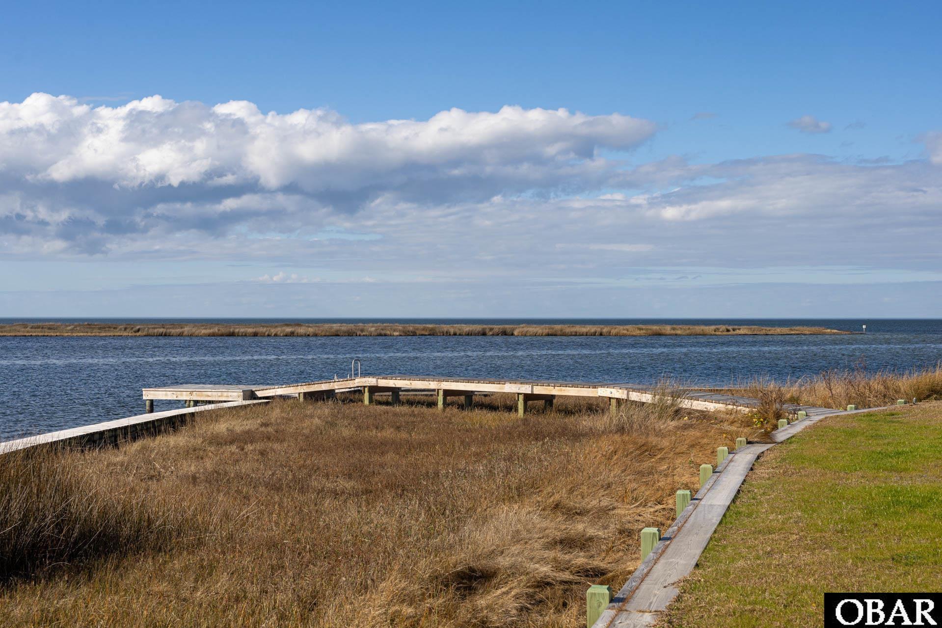 Waterfront lot with a wooden boardwalk and dock extending through marsh grass toward open water.