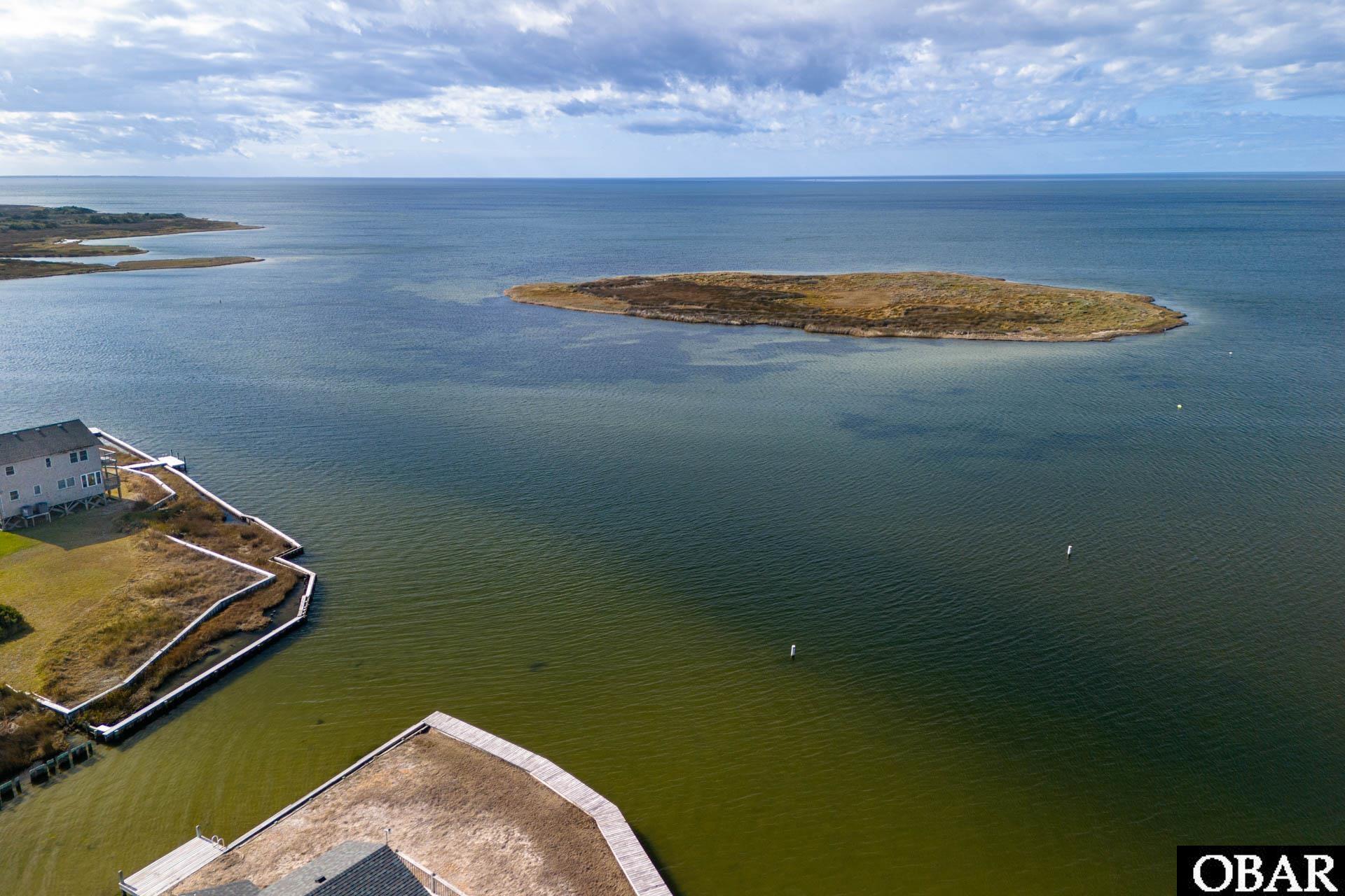 Aerial view of an undeveloped island lot surrounded by water, near waterfront homes and docks.