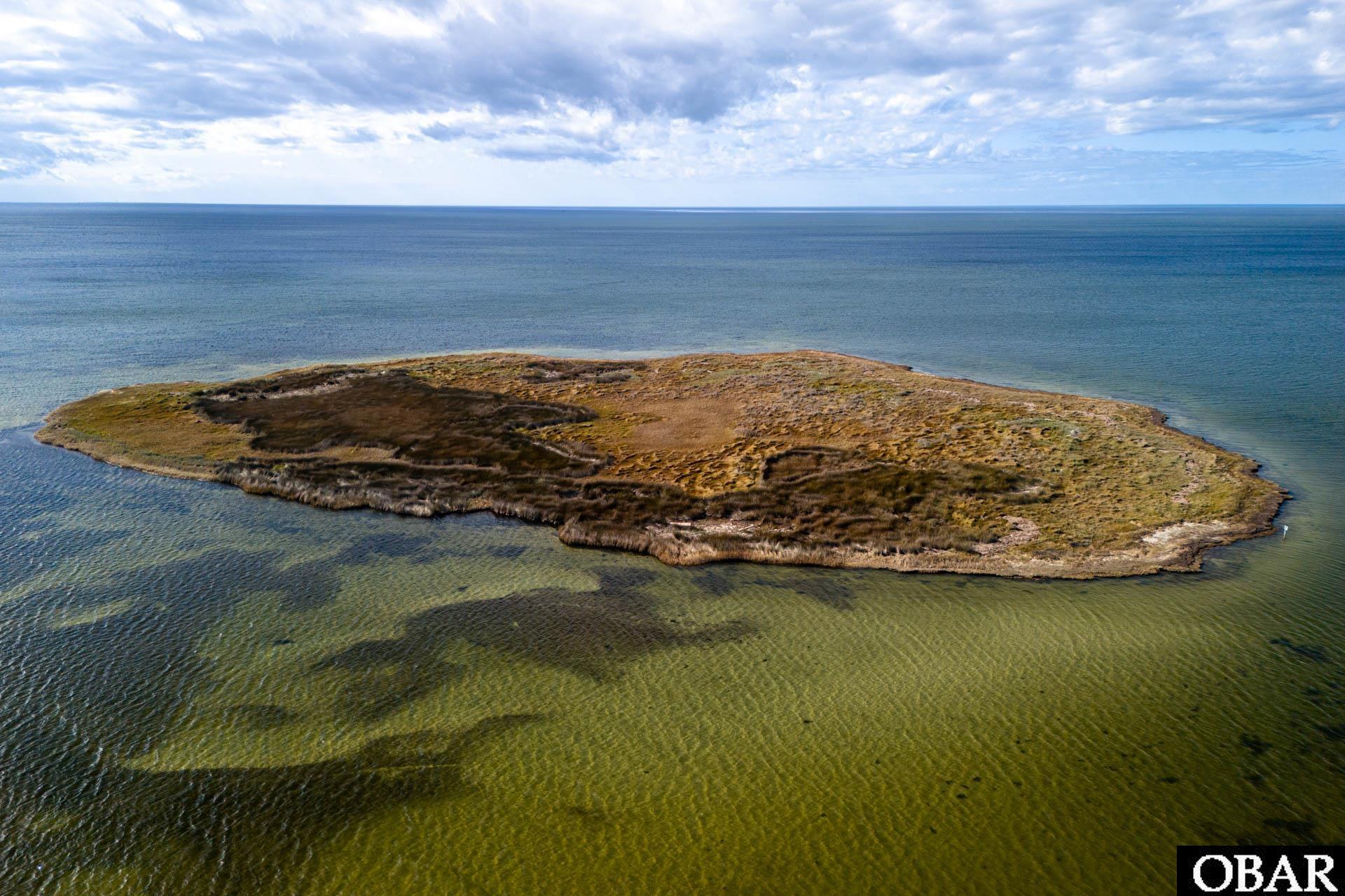 Aerial view of an undeveloped island lot surrounded by shallow water and open sea.