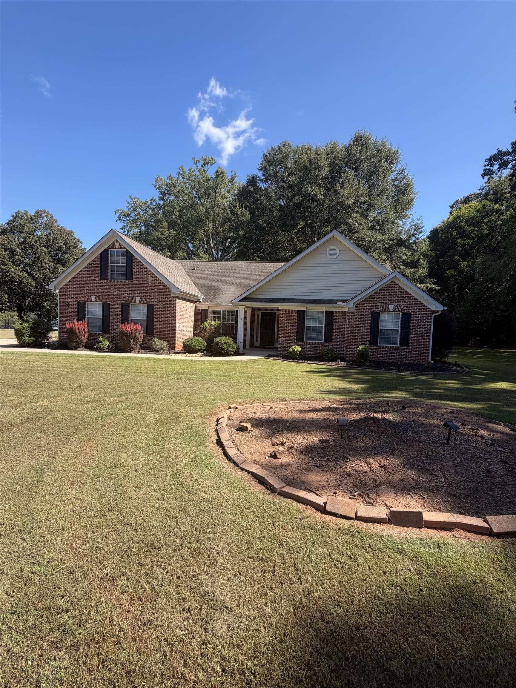 Single-story brick house with gabled roof, broad lawn, and curved brick-edged planting bed.