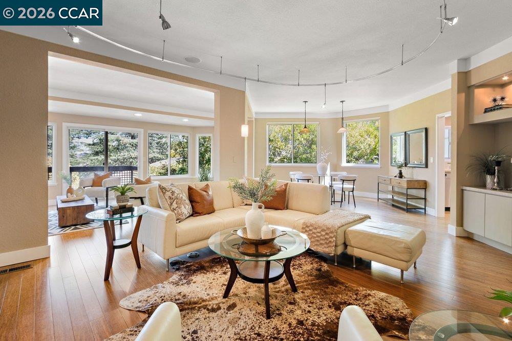 Open-plan living room with a cream sectional, glass coffee tables, and large windows overlooking trees.