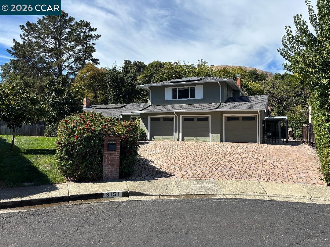 Gray two-story house with three-car garage and broad brick-paver driveway.