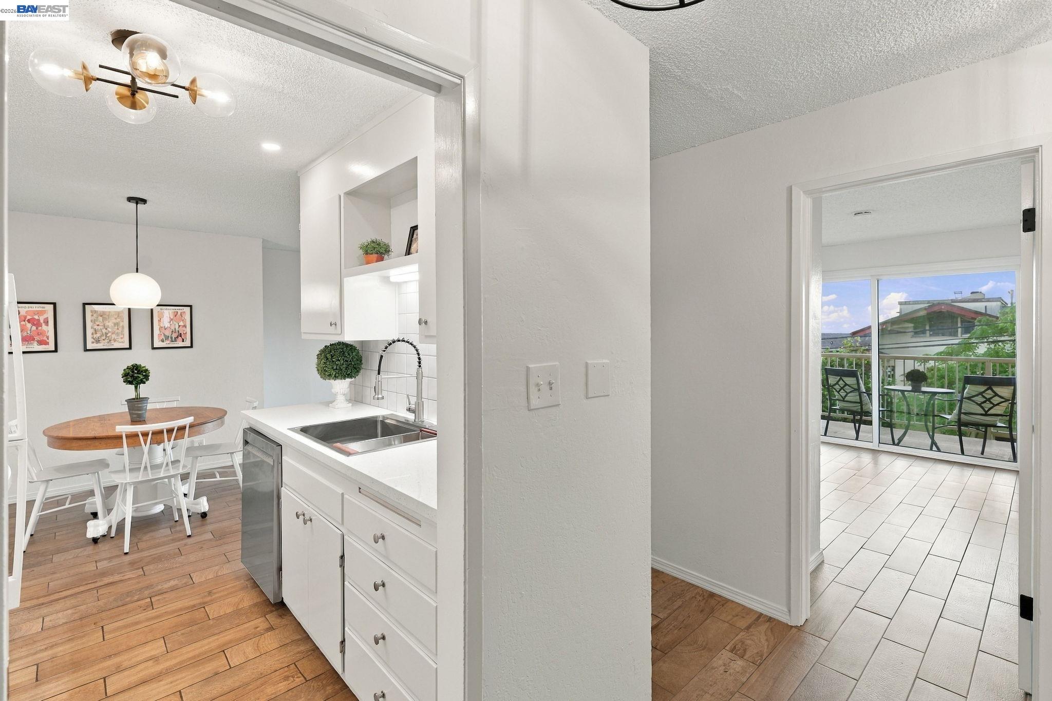 Bright kitchen and dining area with white cabinetry, wood floors, and a balcony visible through the doorway.