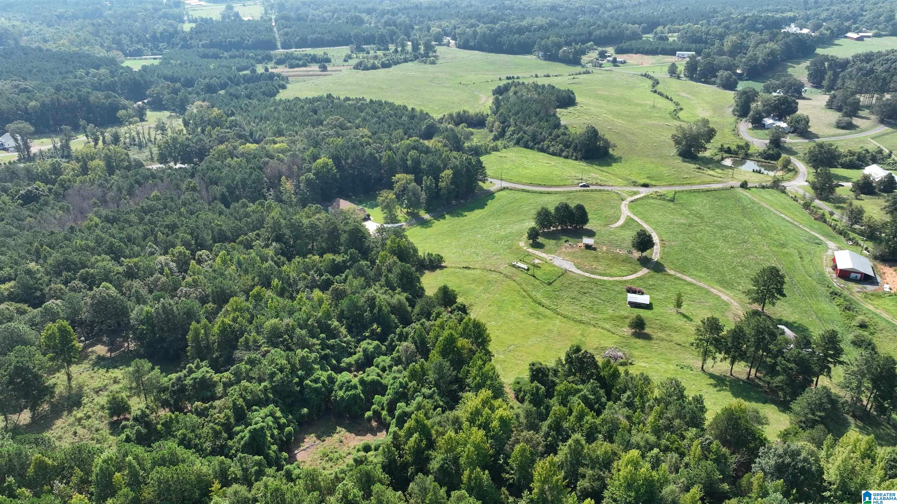 Aerial view of open fields and wooded acreage with a winding driveway and several outbuildings.