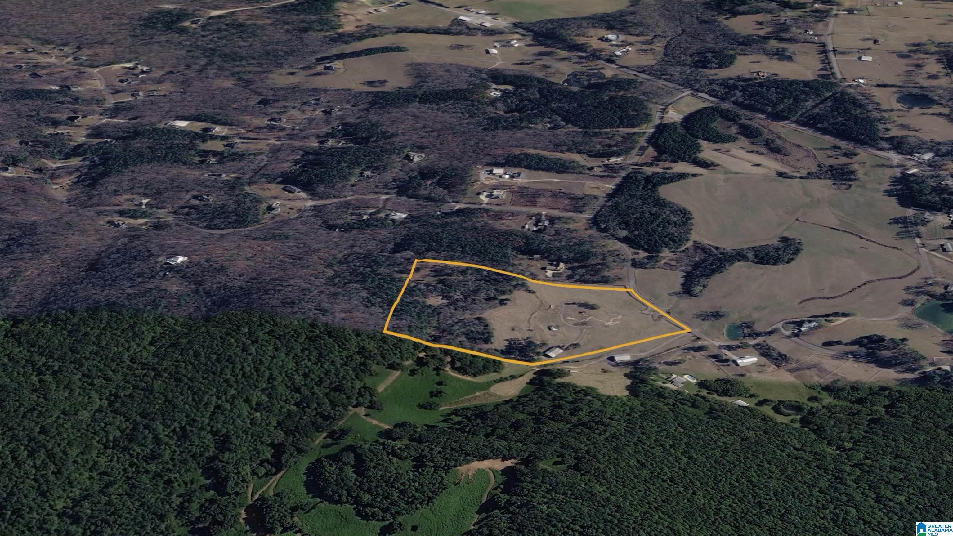 Aerial view of a rural property outlined in yellow, with open land bordered by woods.