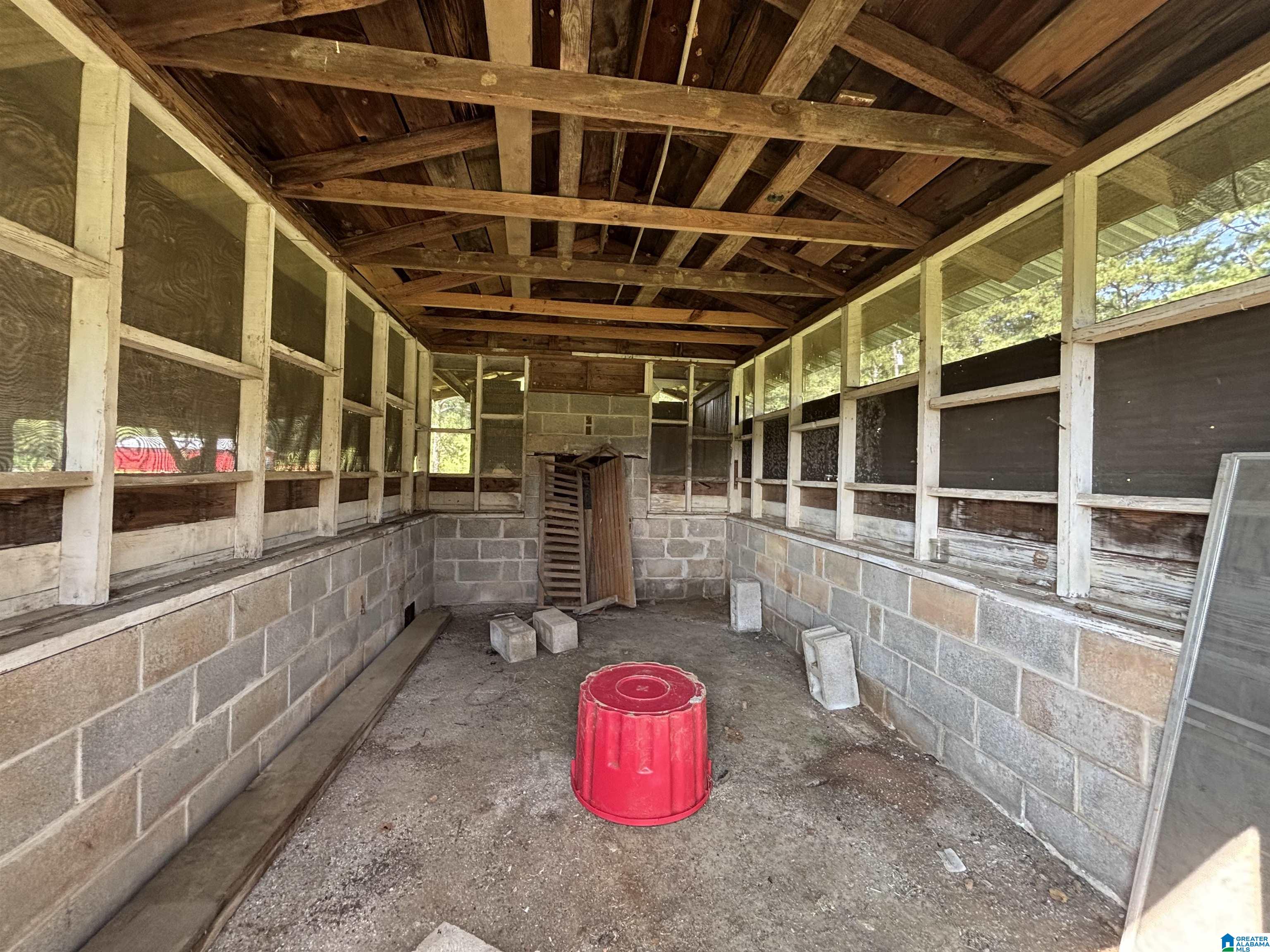 Rustic outbuilding interior with exposed timber rafters, screened walls, cinder-block sides, and a red tub.