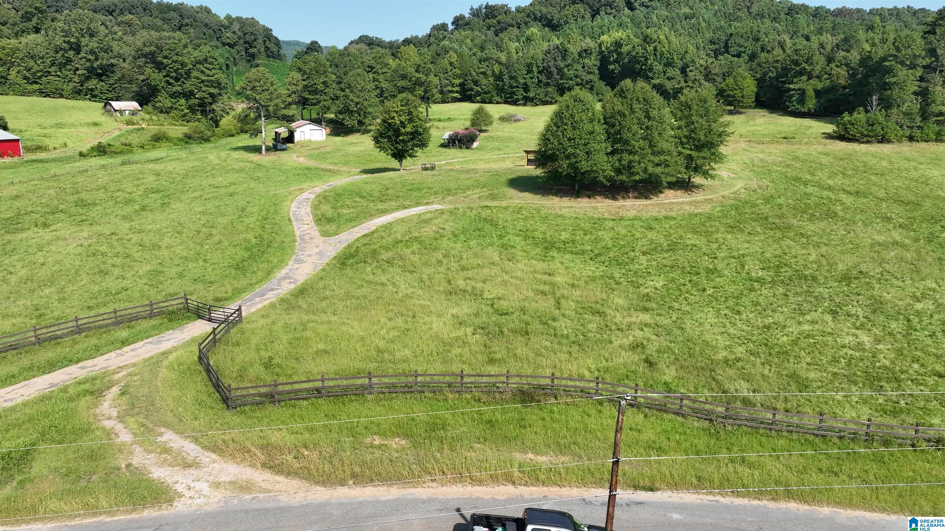 Aerial view of fenced pasture with a winding path, scattered trees, and small outbuildings.