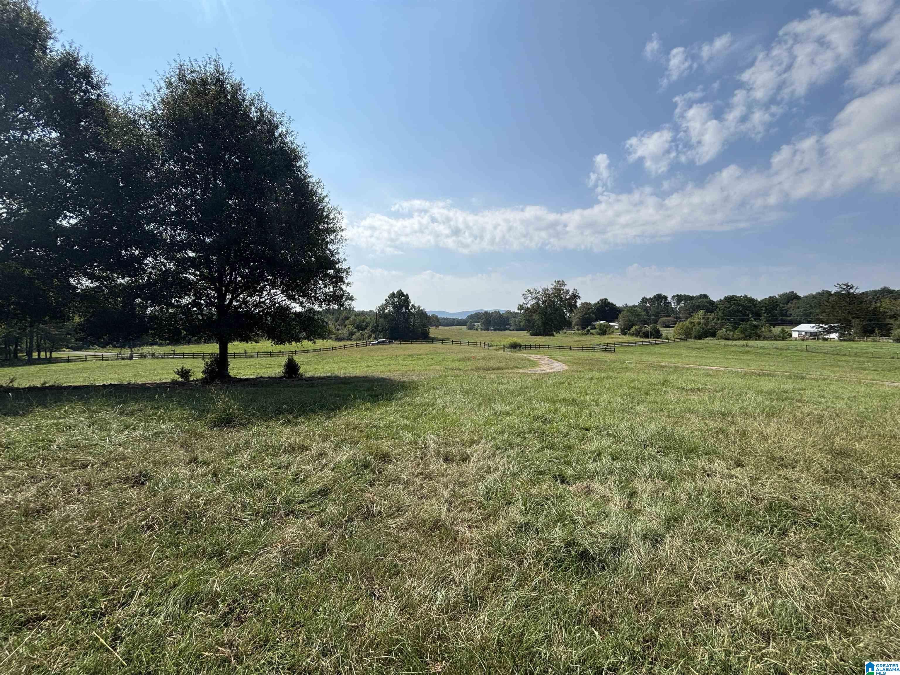 Open grassy property with split-rail fencing, a large shade tree, and distant hills.