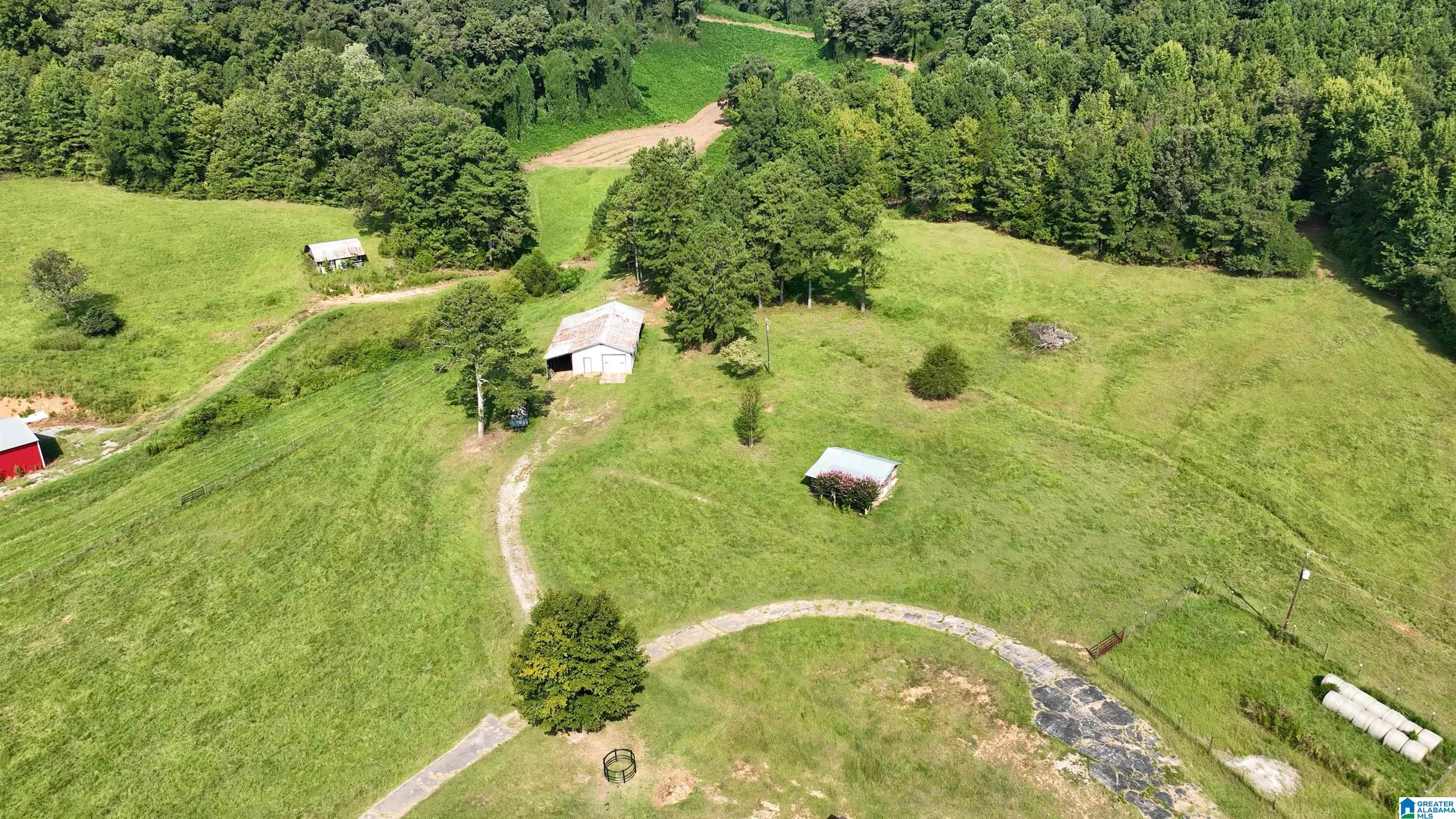 Aerial view of grassy rural acreage with several outbuildings, curving drives, and surrounding woods.