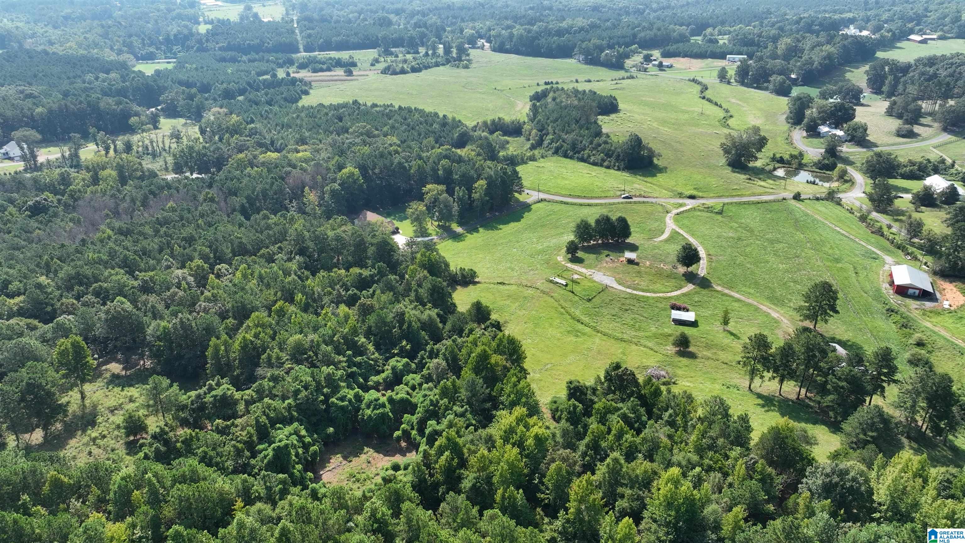 Aerial view of open pasture and wooded land with a winding drive and red barn.