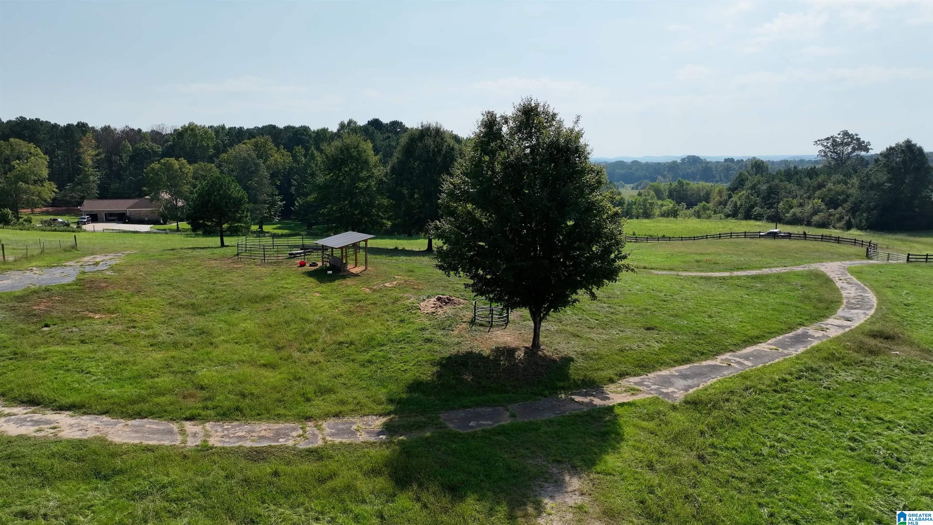 Aerial view of a rural pasture with fenced paddocks, a covered shelter, and a curving paved path.