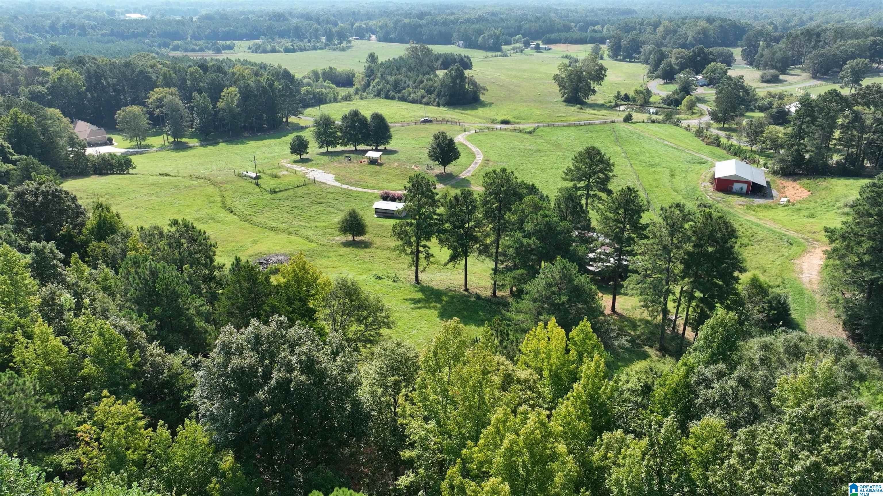 Aerial view of fenced green pasture, wooded acreage, and a red barn.