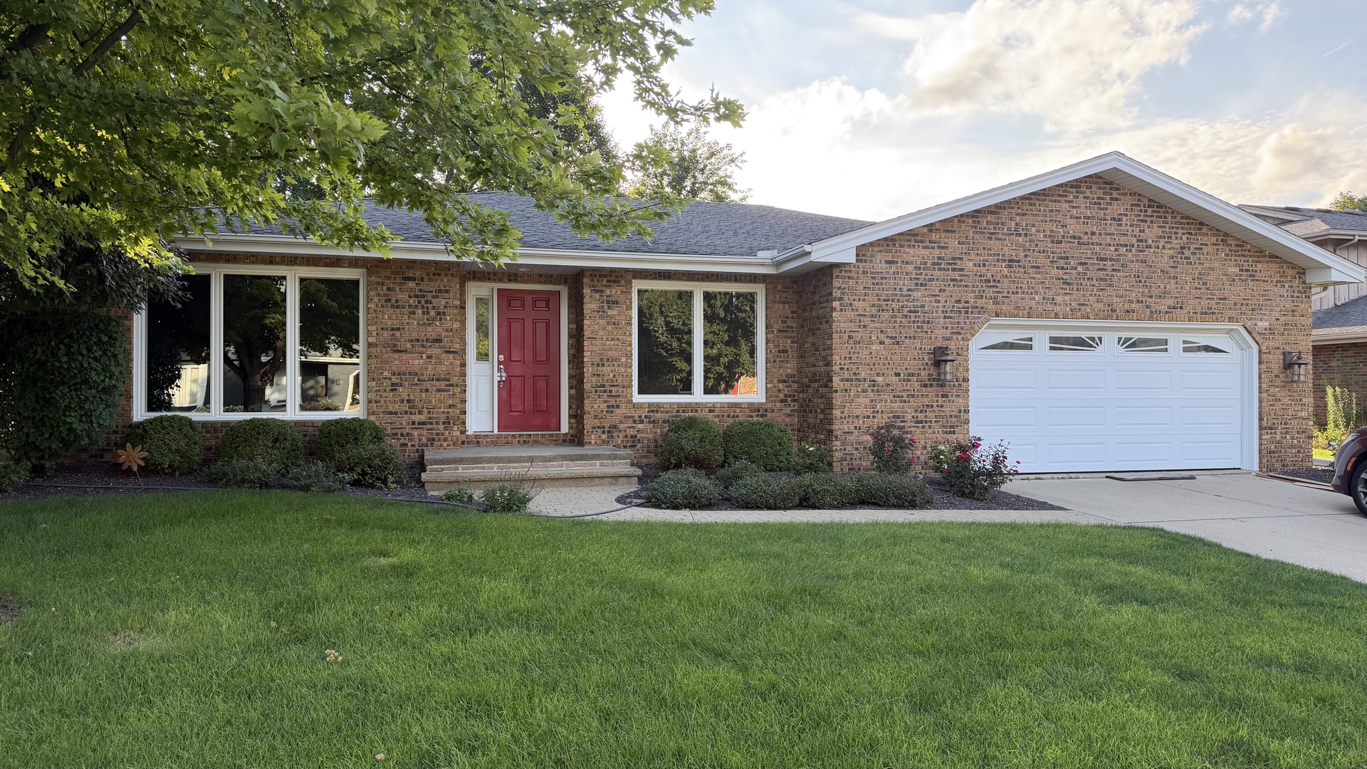 Single-story brick home with a red front door, white garage, and broad green lawn.