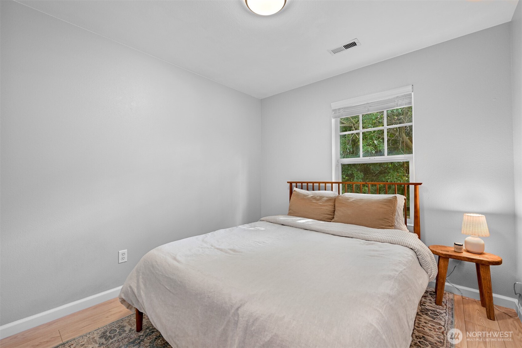Bedroom with a large bed beneath a window overlooking leafy greenery.