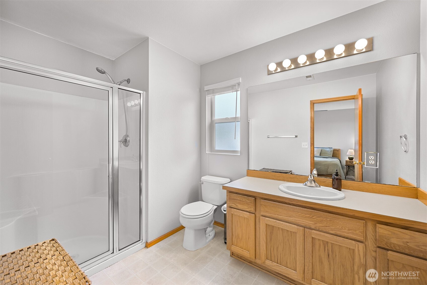 Bathroom with a glass shower, oak vanity, large mirror, and window.