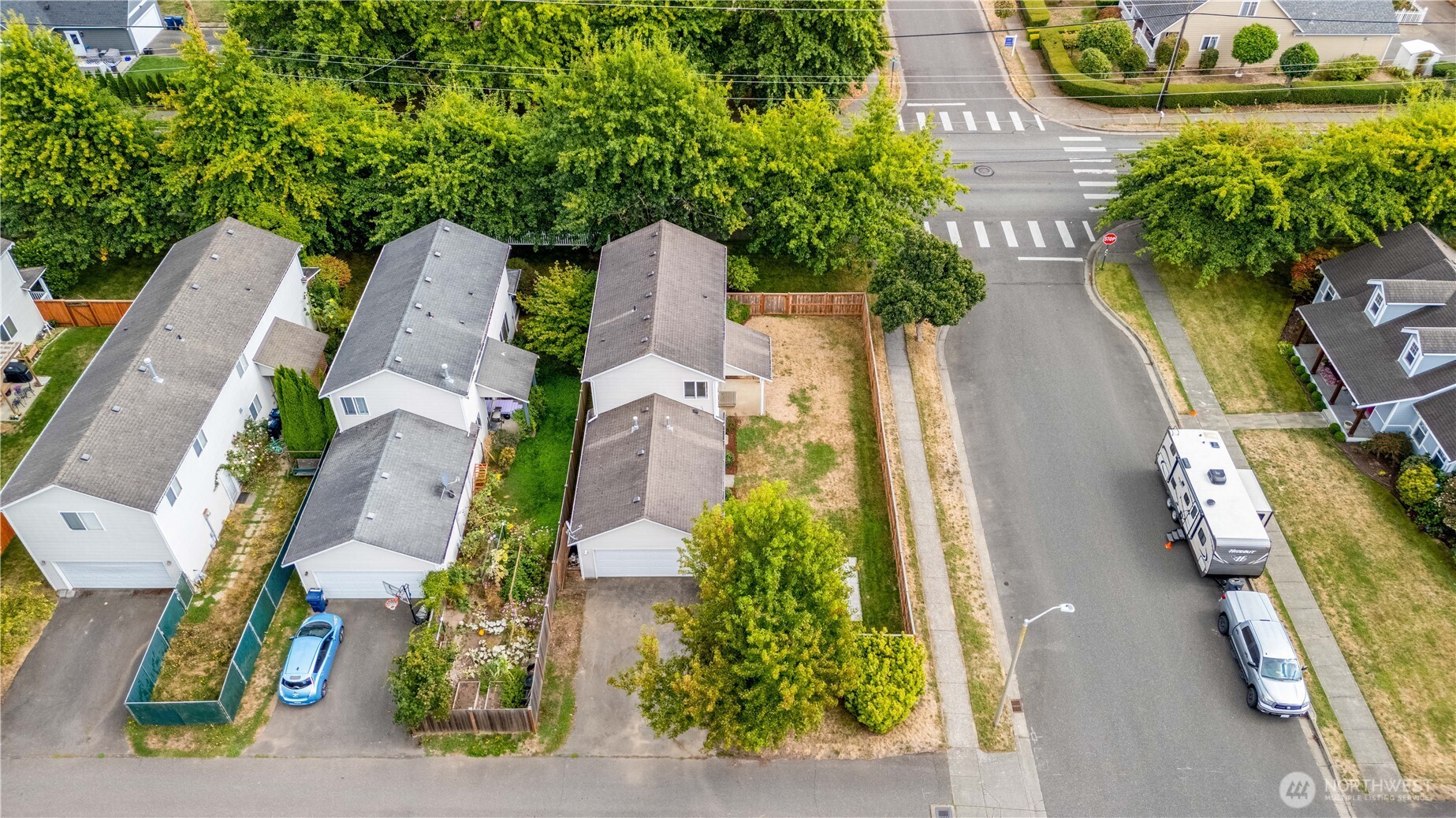 Aerial view of a home with a fenced dry backyard beside a residential street and intersection.