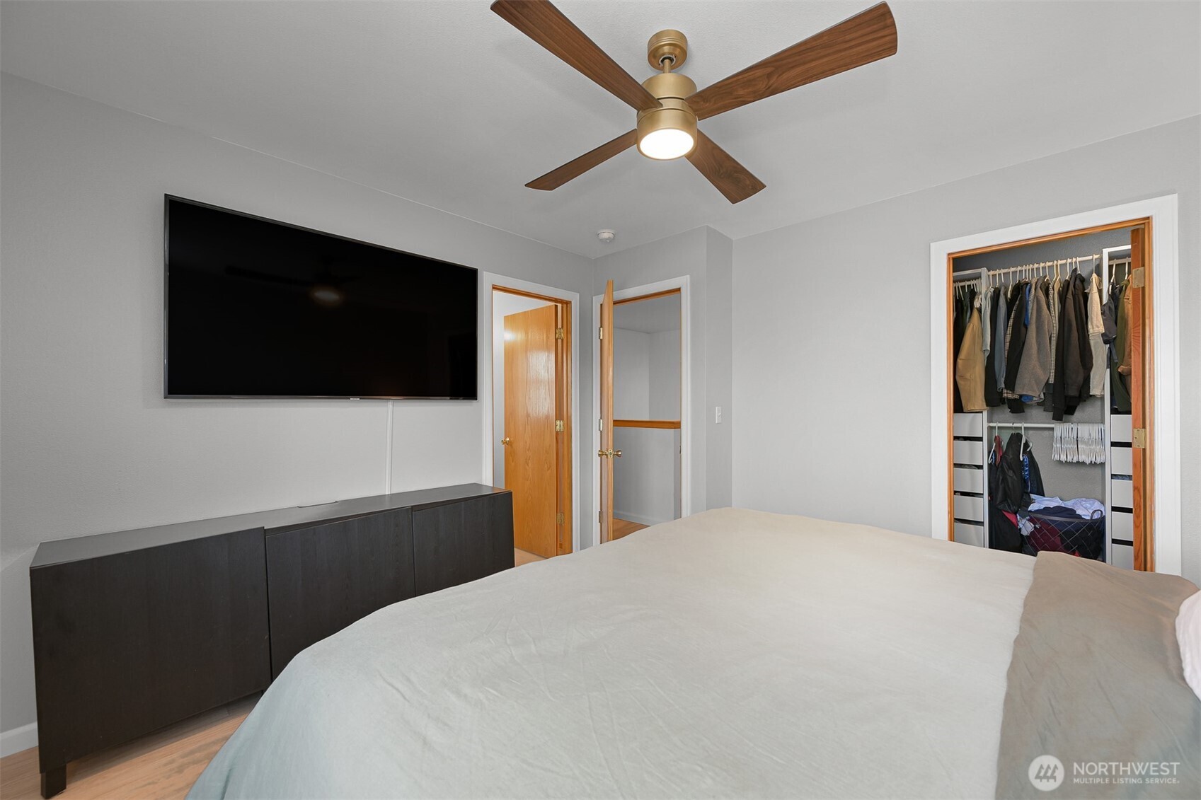 Bedroom with a wall-mounted TV, wood-blade ceiling fan, and open closet.