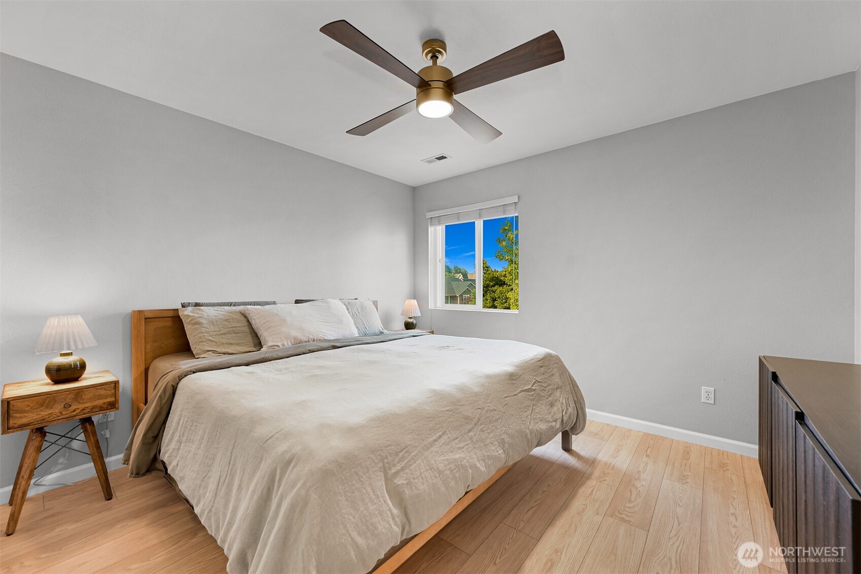 Bedroom with a large neutral-toned bed, wooden bedside table, and ceiling fan.