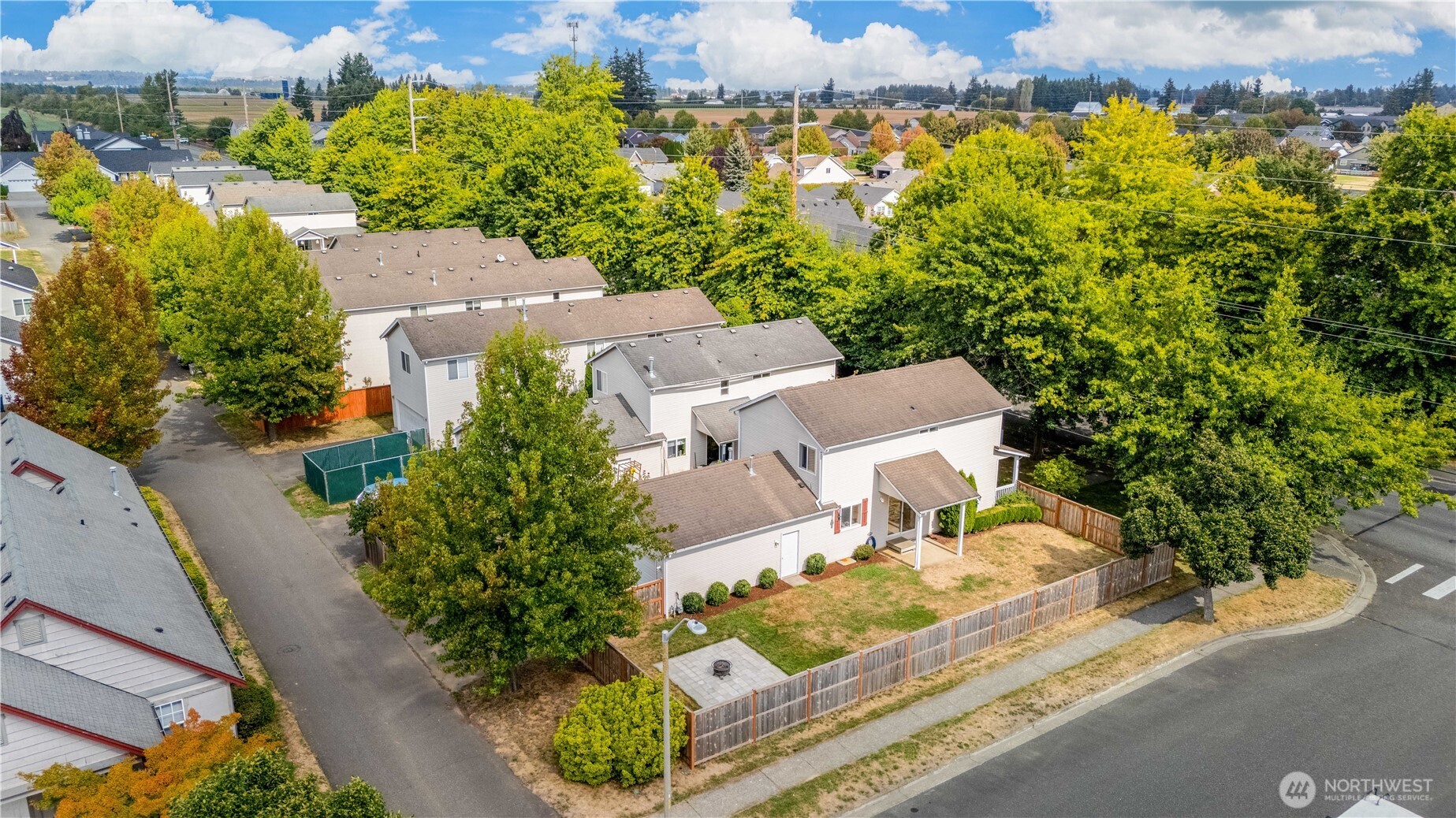 Aerial view of a home with a fenced backyard, patio, and autumn trees.