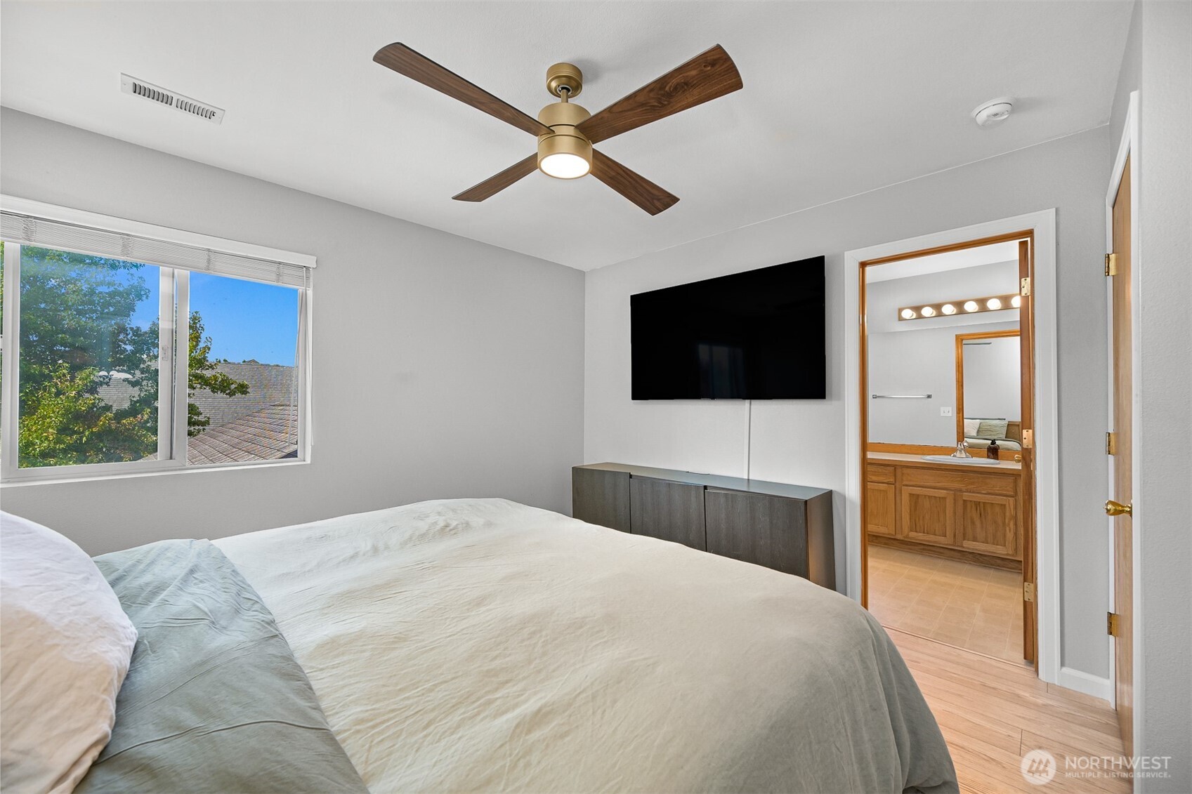 Bedroom with a wood-blade ceiling fan, wall-mounted TV, and doorway to an adjoining bathroom.