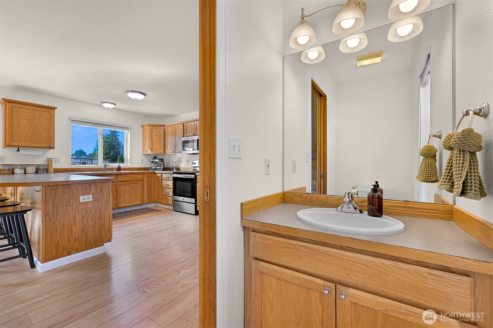 Bathroom vanity with wood cabinetry and oval sink, with the kitchen visible through the doorway.