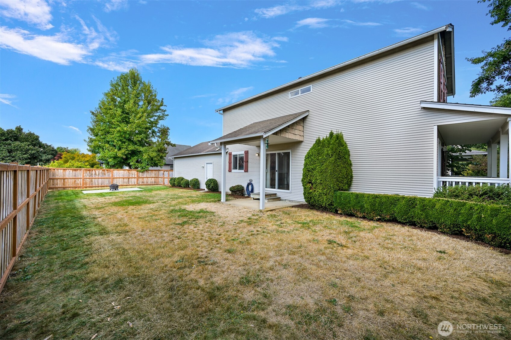 Two-story home with a covered patio and fenced backyard with lawn and shrubs.