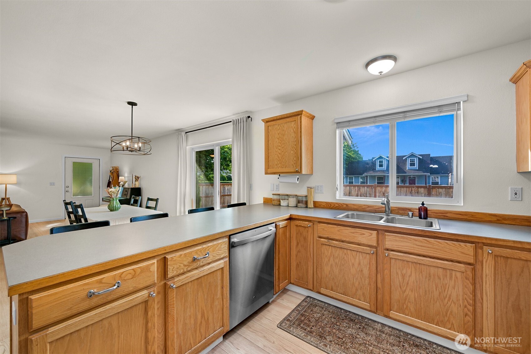 Kitchen with honey-colored wood cabinets, a stainless steel dishwasher, and a window above the sink.