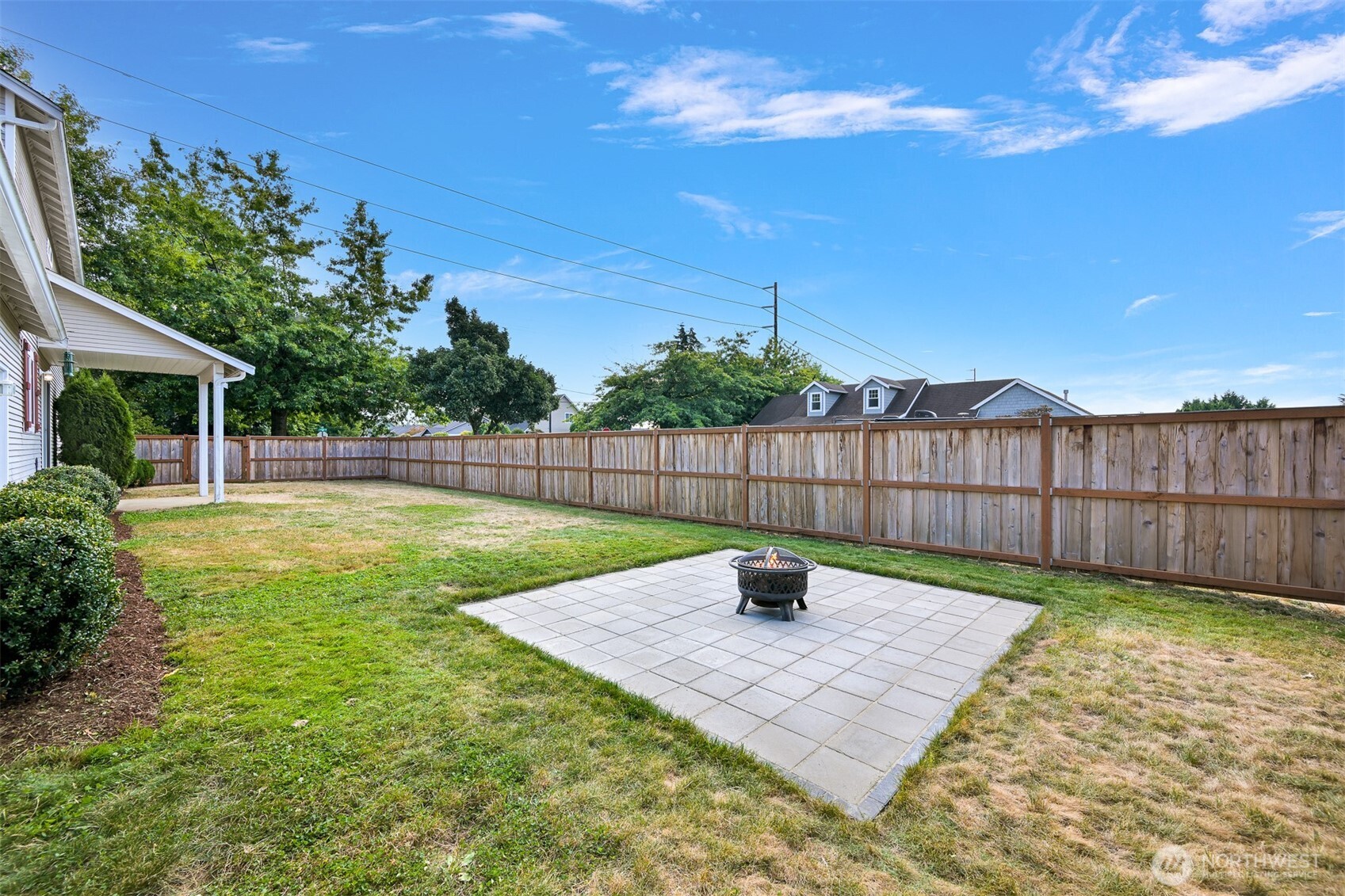 Fenced backyard with a paved fire-pit patio, lawn, and covered porch.