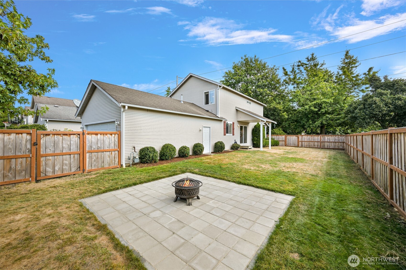 Home’s fenced backyard with a paved patio and fire pit.