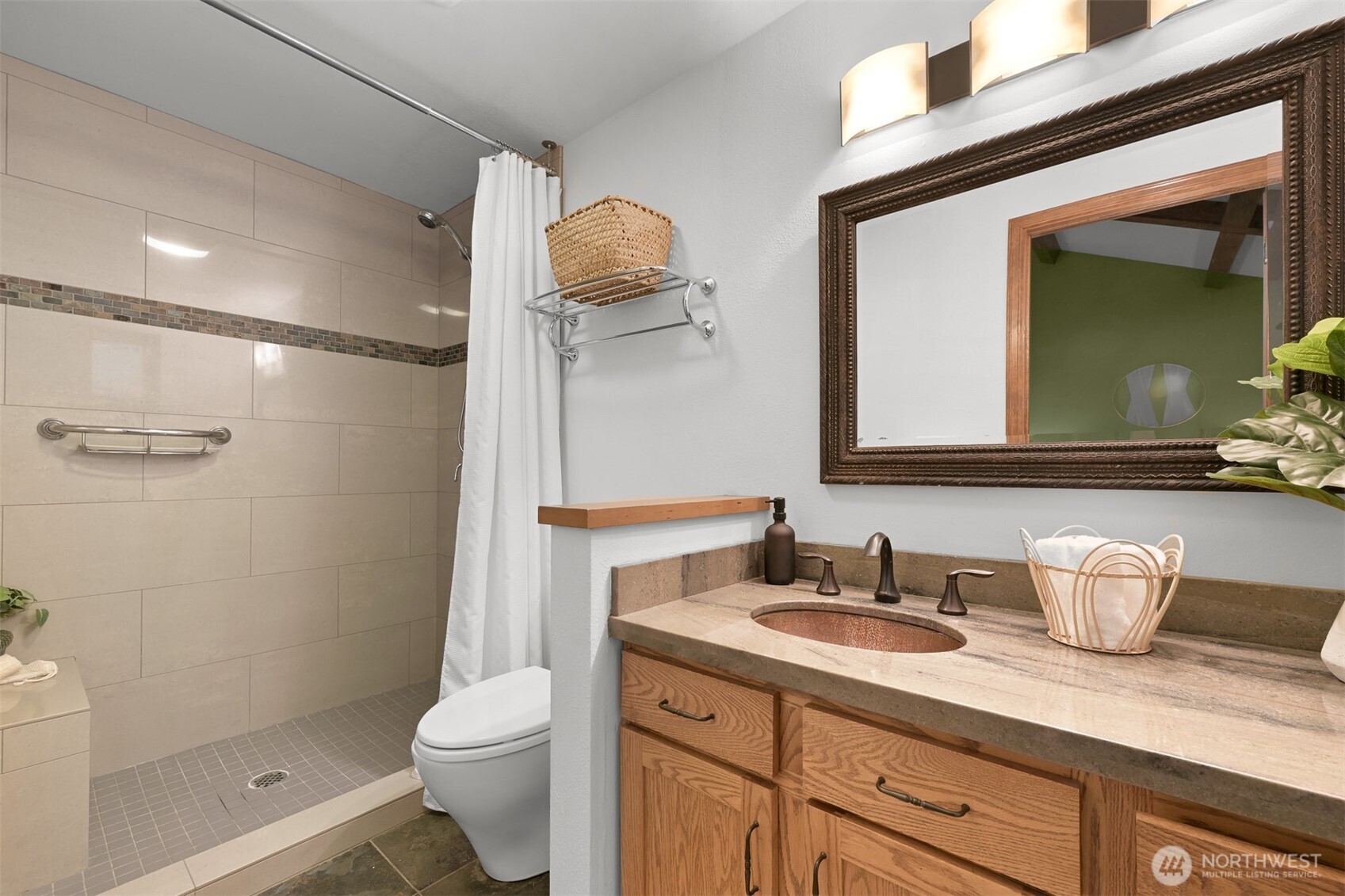 Bathroom with a tiled walk-in shower and wood vanity topped by a stone counter and copper-toned sink.