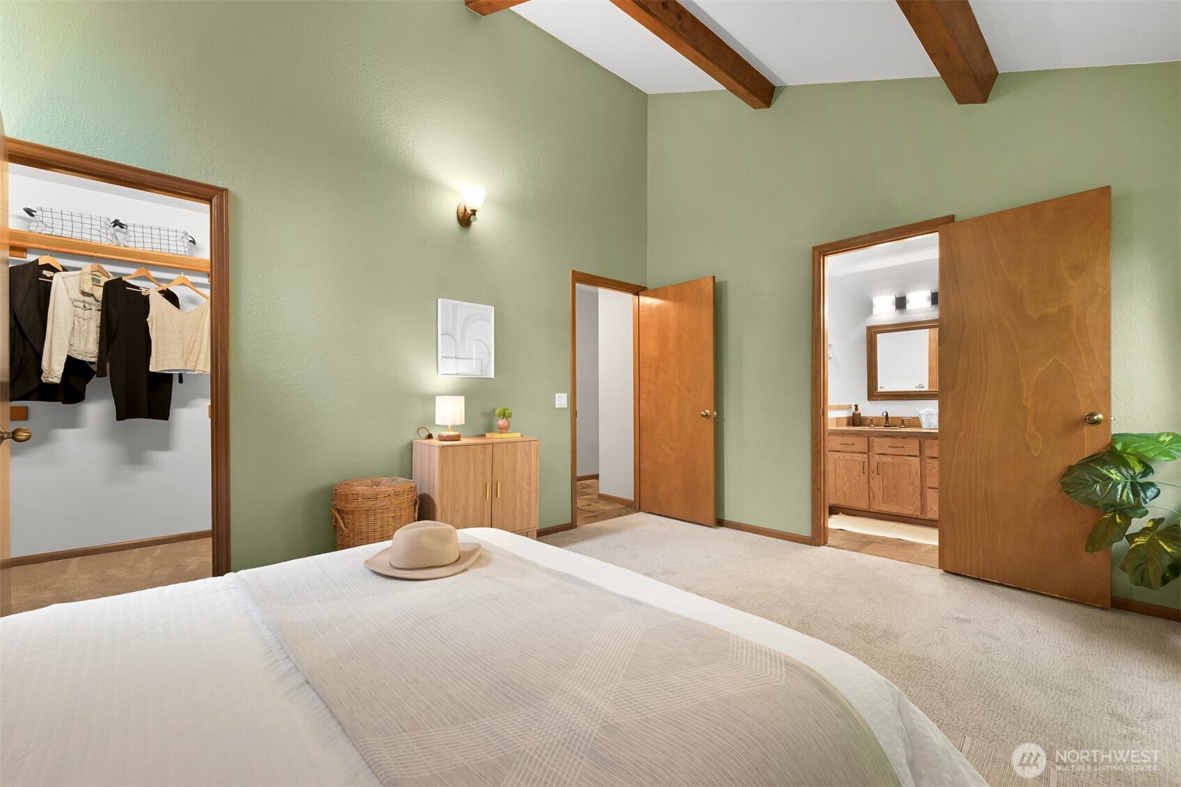 Bedroom with sage-green walls, exposed wood beams, and open access to a closet and bathroom.