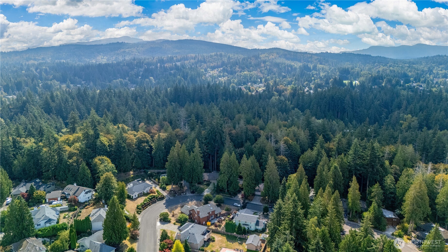 Aerial view of a wooded neighborhood with distant mountain ridges and scattered homes.