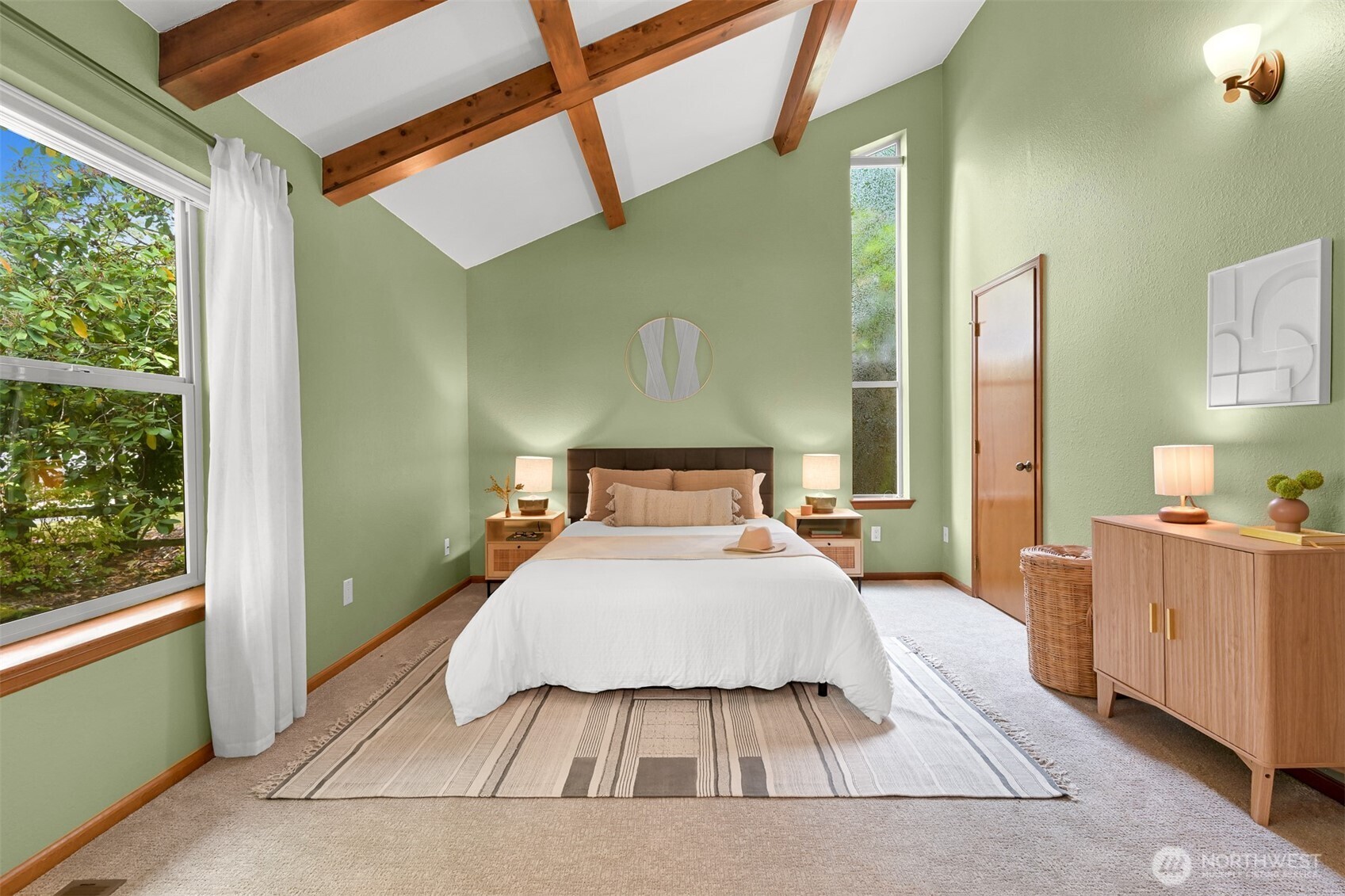 Staged bedroom with sage-green walls, exposed wood beams, and a white bed between large windows.