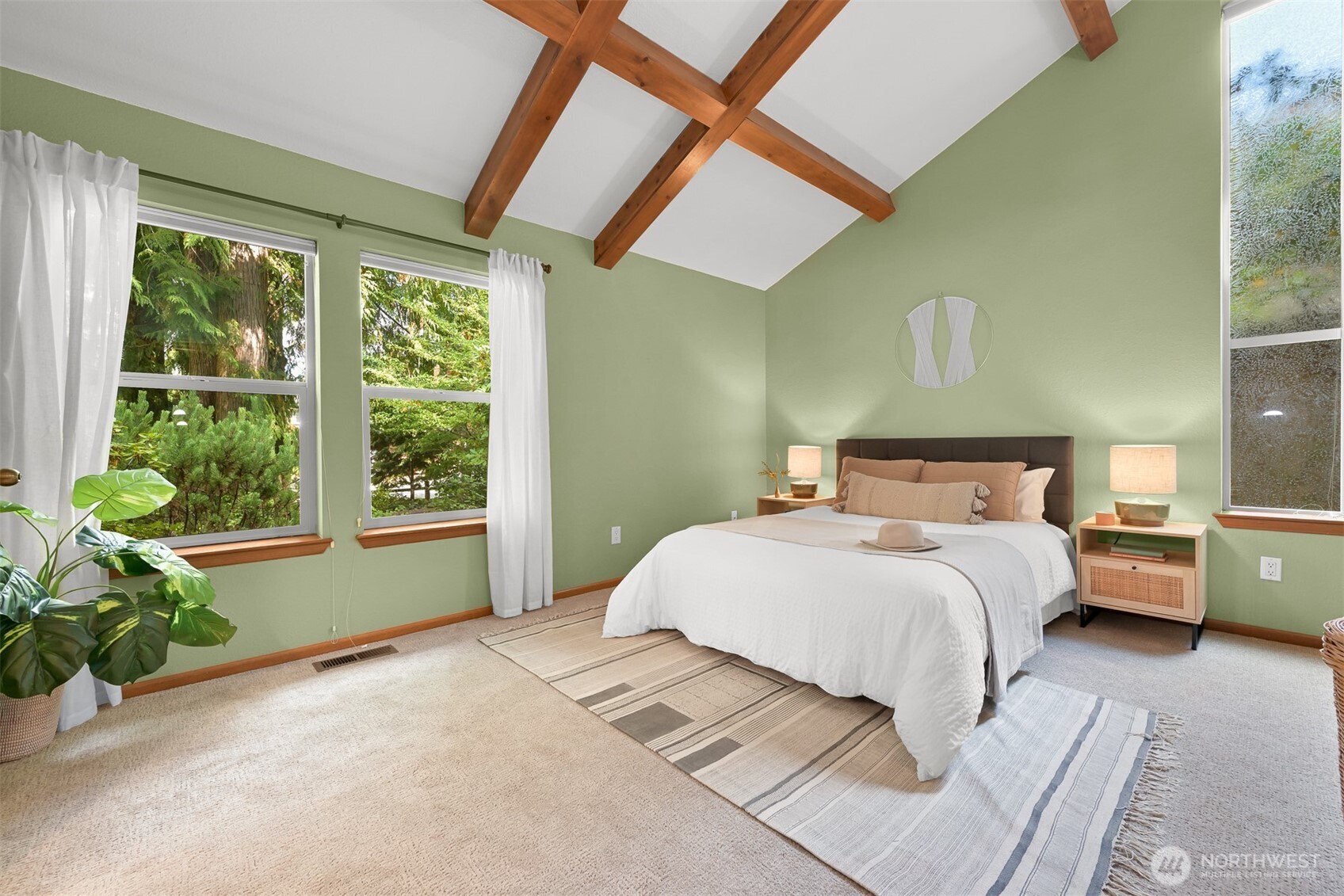 Bedroom with exposed wood ceiling beams, pale green walls, and large windows overlooking trees.