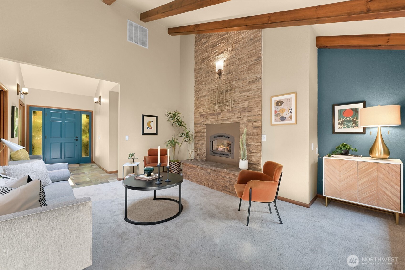 Living room with a stone fireplace, exposed wood beams, and a teal entry door.