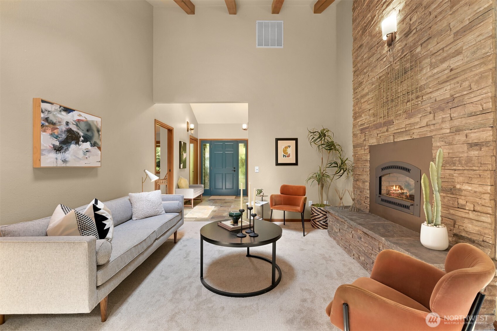 Living room with vaulted wood-beam ceiling, stone fireplace, and blue front door.