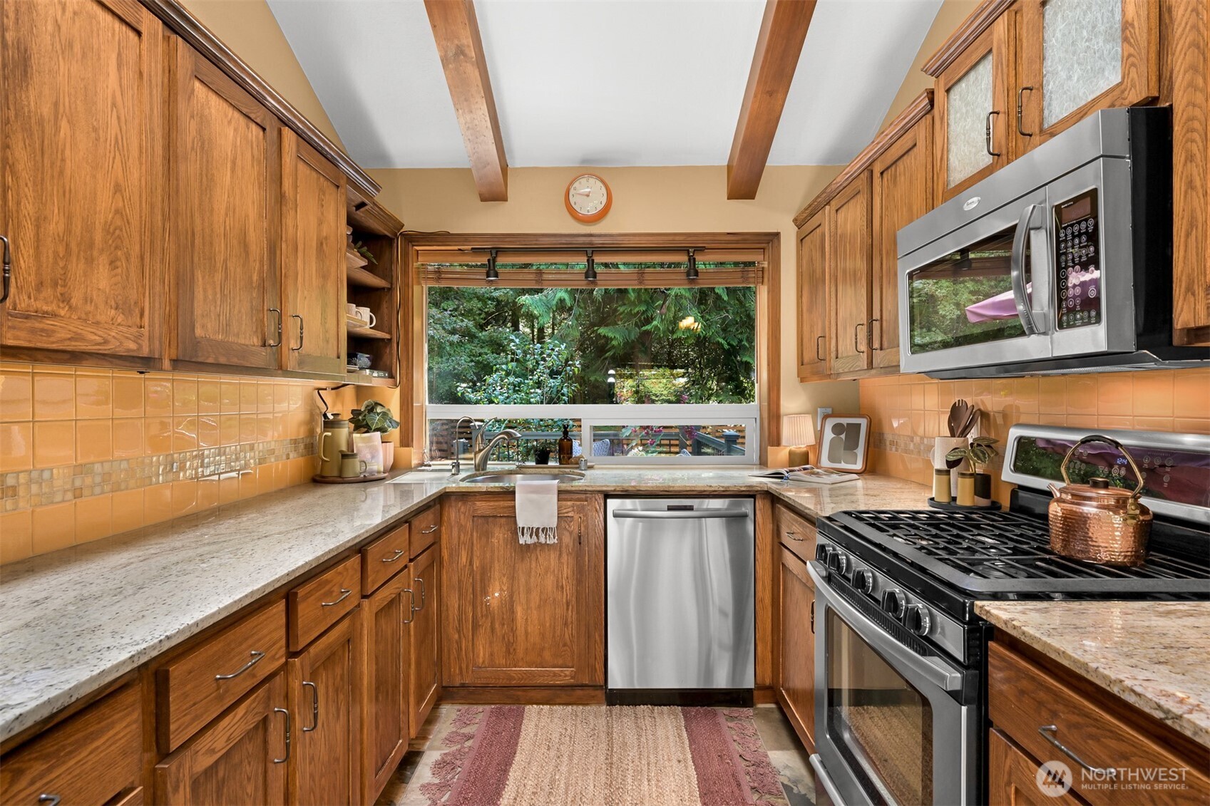 Kitchen with wood cabinets and peach tile, featuring a wide garden-facing window above the sink.