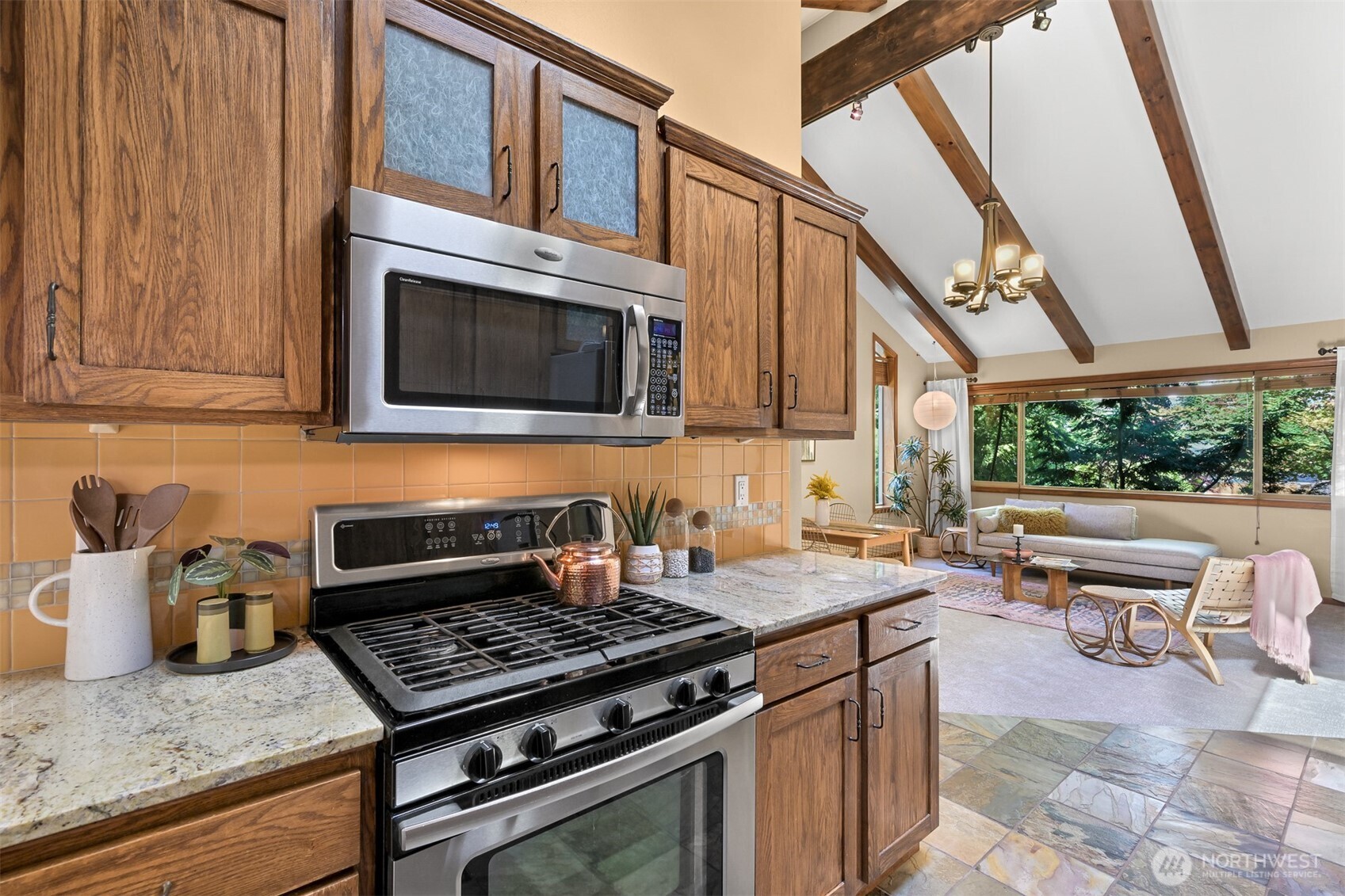 Kitchen with oak cabinets and stainless appliances opening to a vaulted living room with a large window.