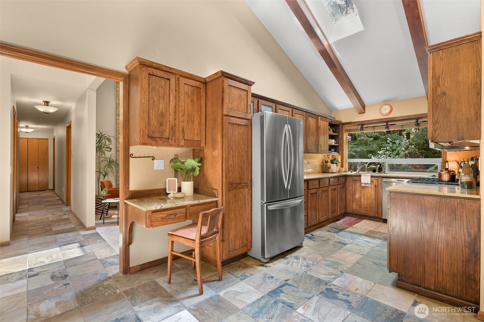 Kitchen with wood cabinetry, stainless steel refrigerator, vaulted ceiling, and multicolored tile floor.