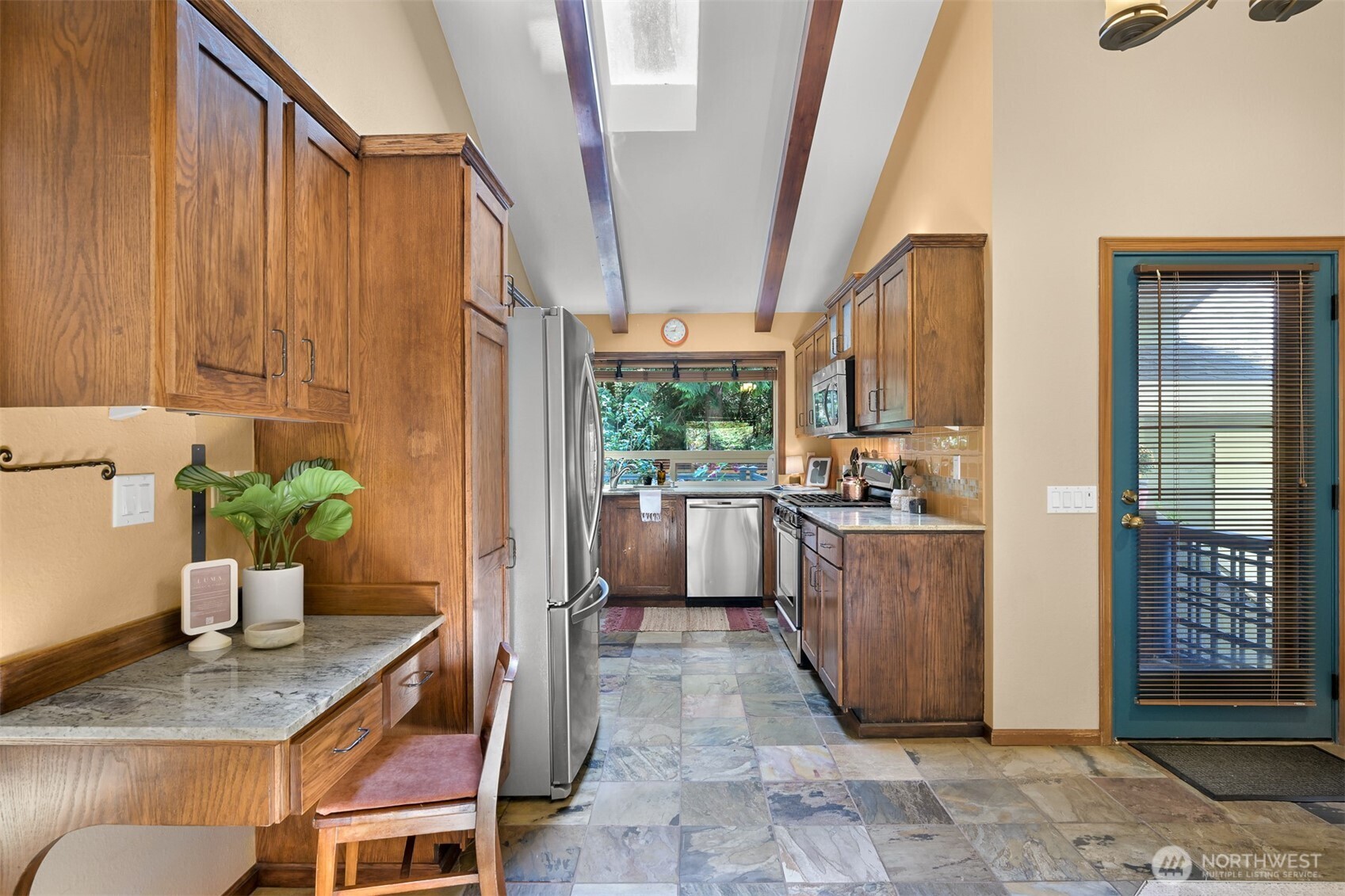 Galley kitchen with warm wood cabinets, stone counters, stainless steel appliances, and a skylight.