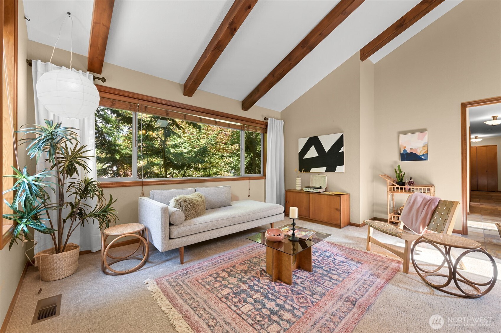 Living room with exposed wood ceiling beams, a wide window, gray sofa, and patterned rug.