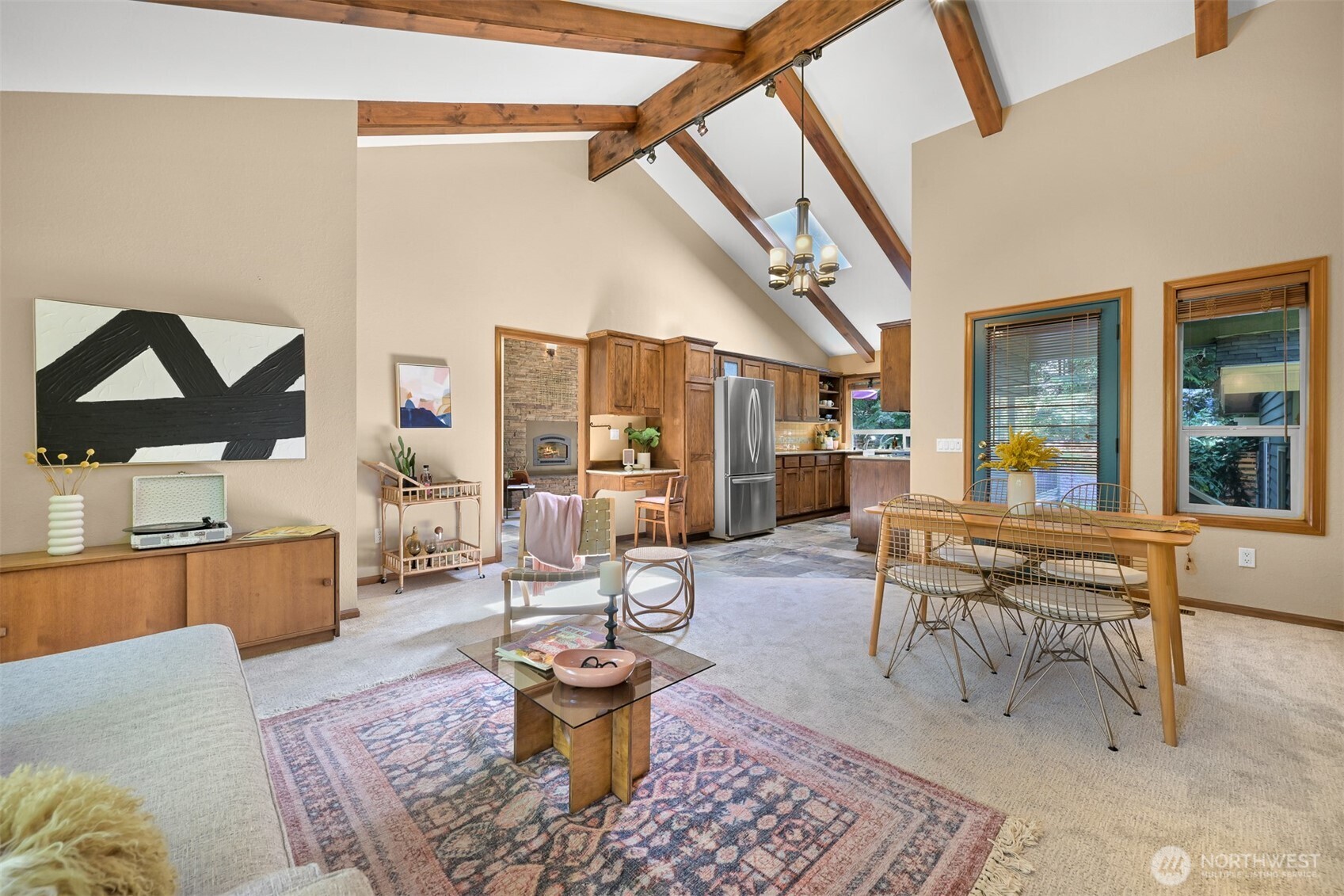 Open-plan living room and kitchen with vaulted wood-beam ceiling, stone fireplace, and dining area.