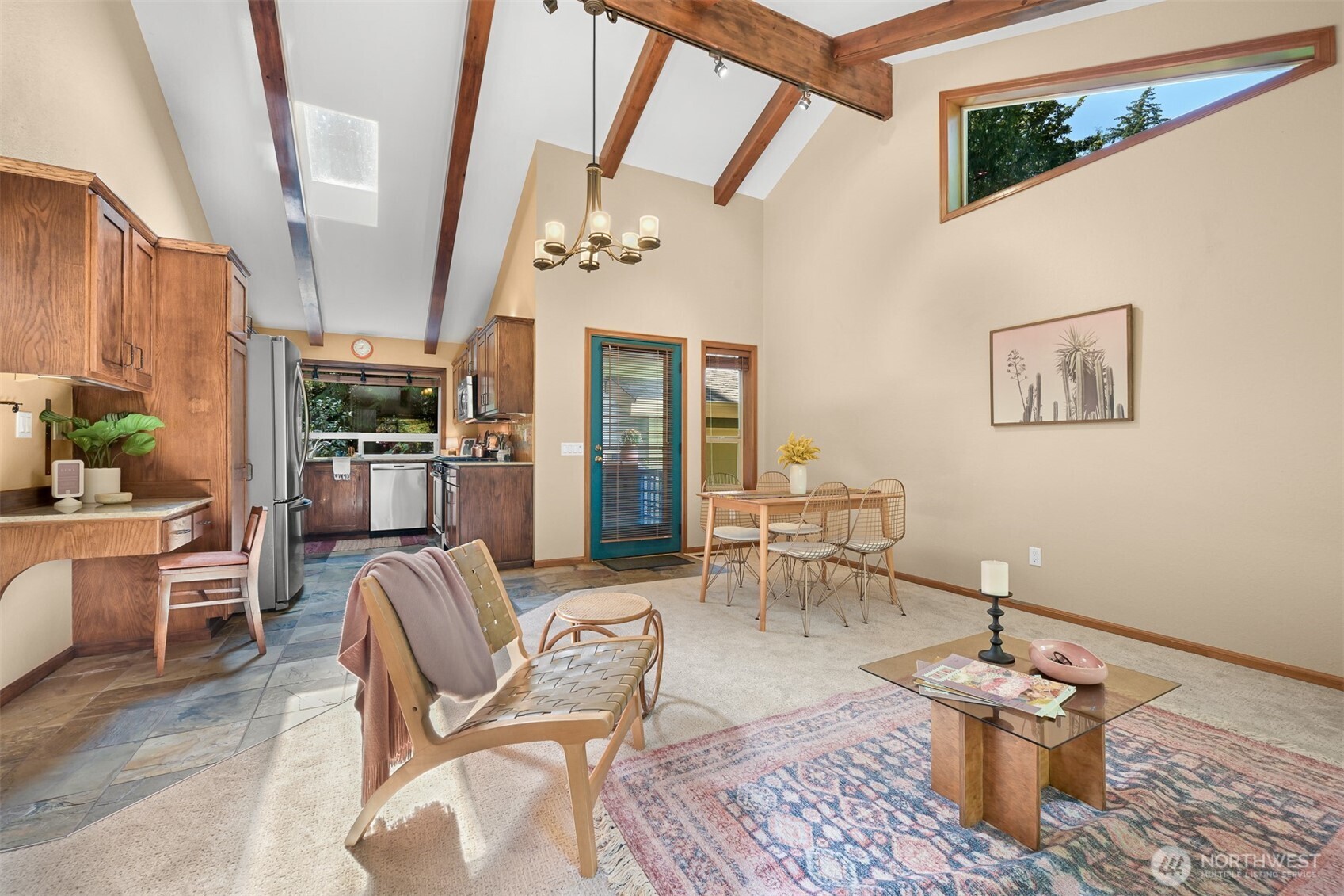 Open living and dining area with exposed wood beams, a high ceiling, and an adjoining wood-cabinet kitchen.