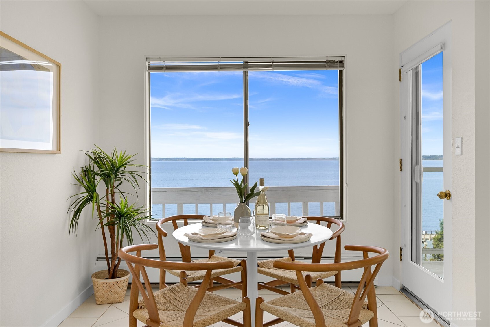 Dining area with a round table and chairs overlooking the water through a large window.
