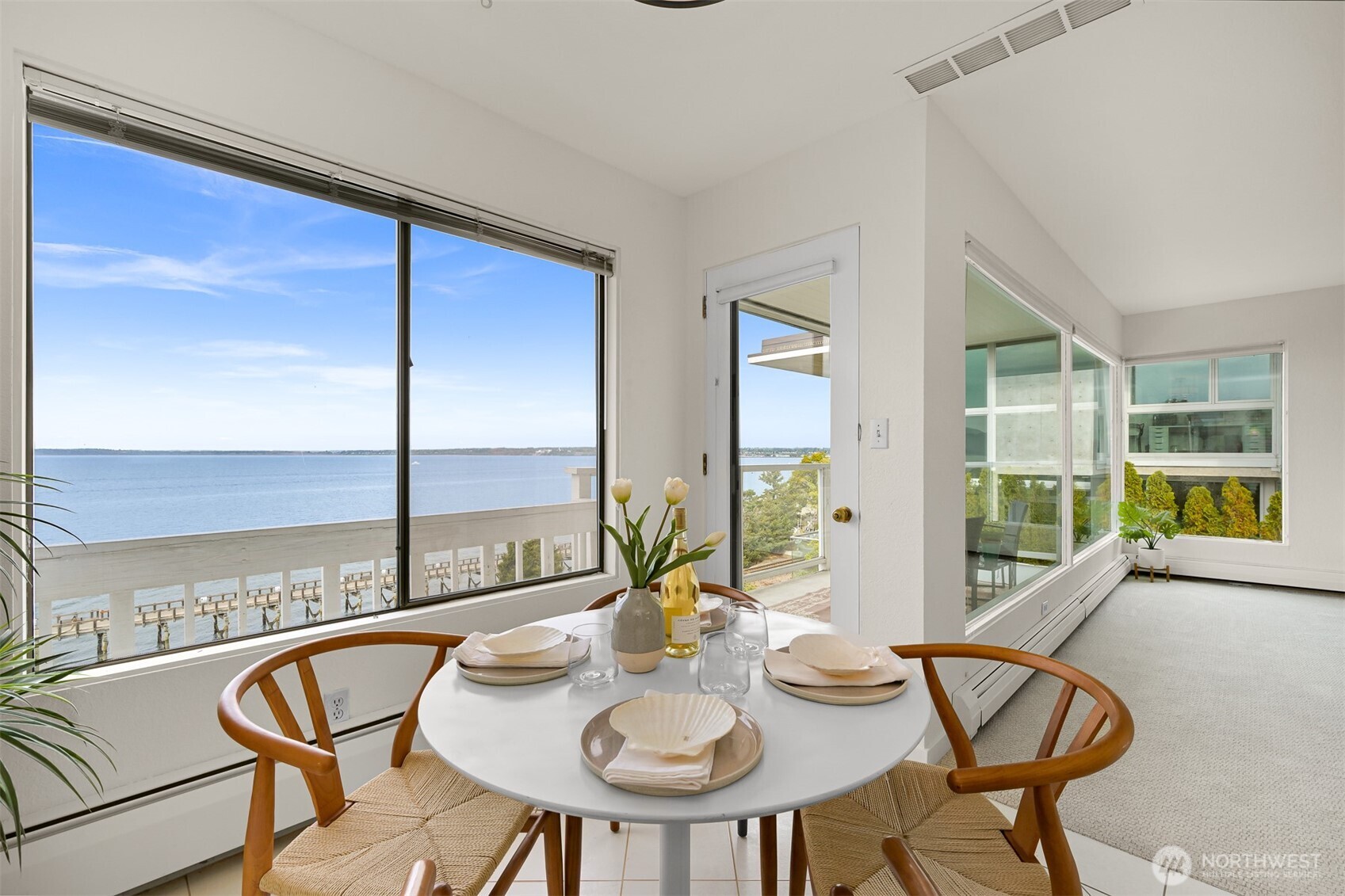 Dining area with a round table beside large windows overlooking the water and a balcony.