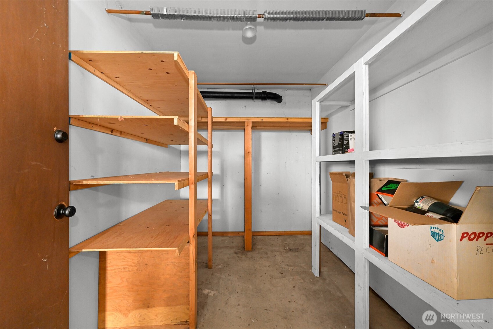 Storage room with wooden and white shelving, boxes, and a concrete floor.