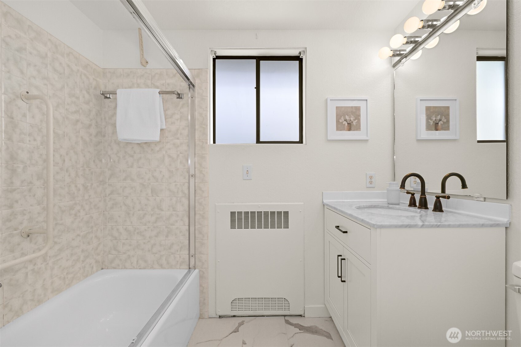 Bathroom with a marble-look tub surround, white vanity, dark bronze fixtures, and window.